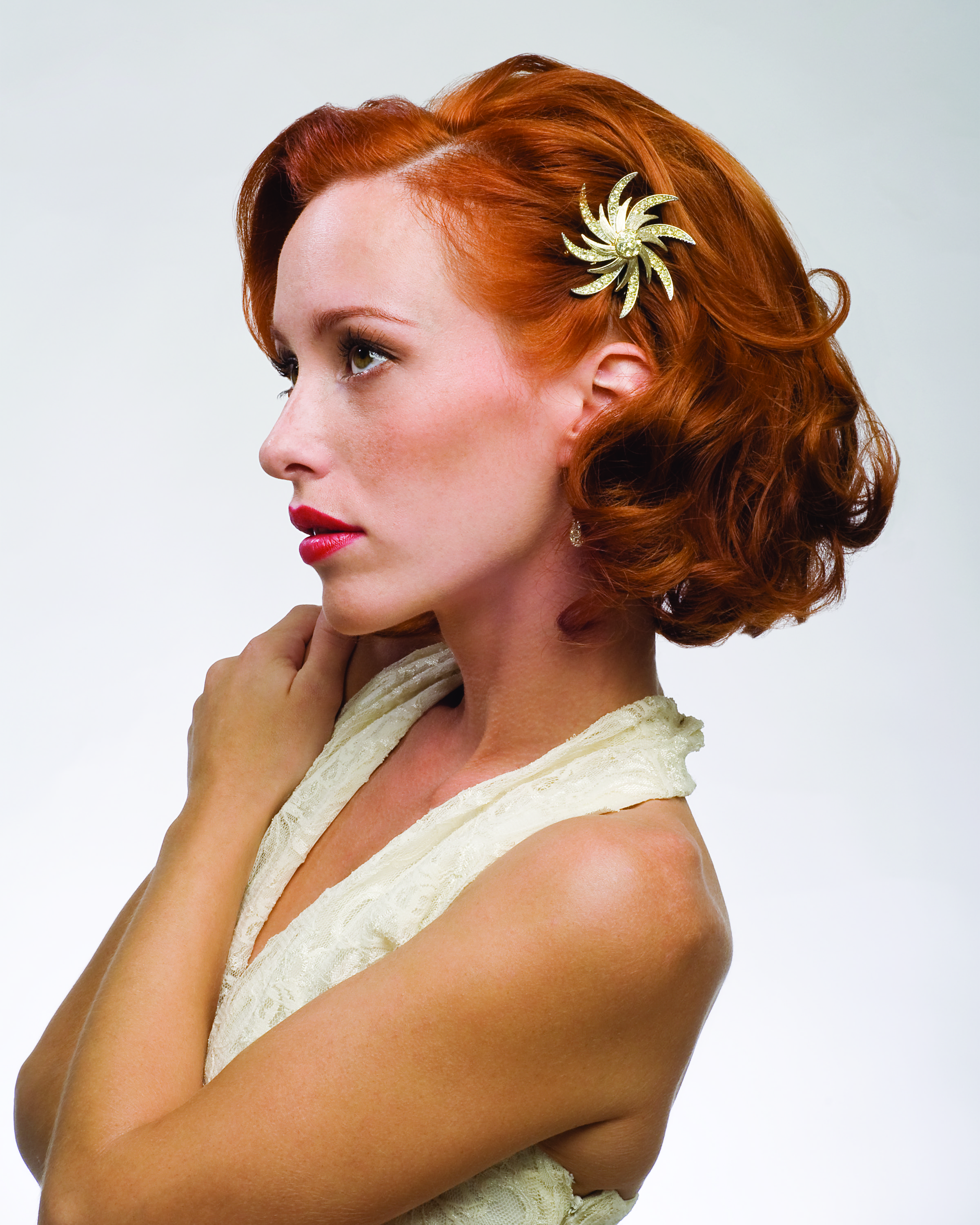 Side profile of Brianna — vintage finger-waved auburn hair with a gold starburst hairpiece, red lipstick, and a cream lace bridal dress. Hair by Angeleah Daidone.